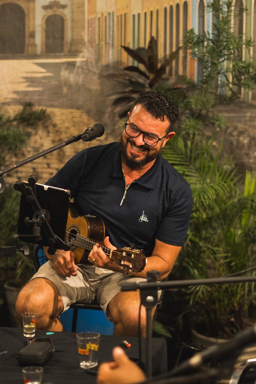 Músico de camisa azul-marinho do Fala Garoto tocando cavaquinho e rindo